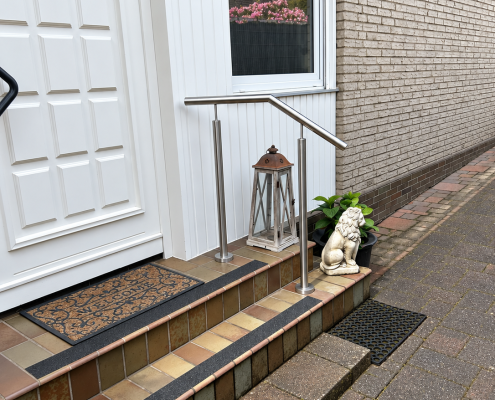 Edelstahlgeländer am Hauseingang mit schwarzen Antirutschstreifen auf den gefliesten Treppenstufen.